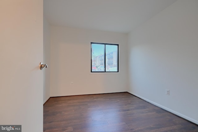 spare room with baseboards and dark wood finished floors