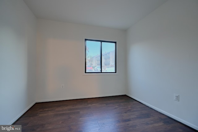 spare room with baseboards and dark wood-type flooring