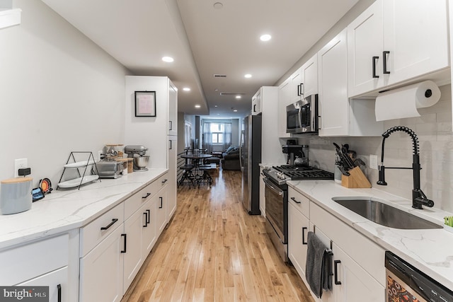 kitchen with stainless steel appliances, white cabinets, a sink, and light stone countertops