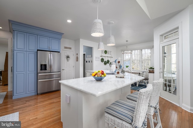 kitchen with a breakfast bar area, blue cabinetry, light wood-type flooring, light stone countertops, and stainless steel fridge