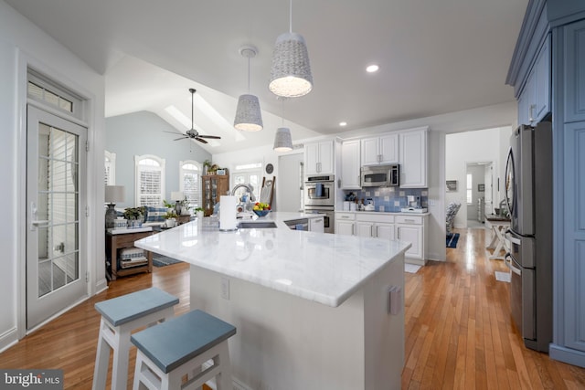 kitchen featuring light wood finished floors, stainless steel appliances, lofted ceiling, decorative backsplash, and a sink