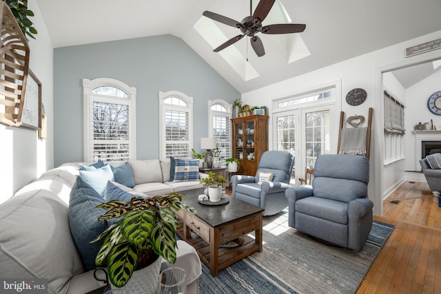 living area featuring a skylight, a ceiling fan, hardwood / wood-style floors, a fireplace, and high vaulted ceiling