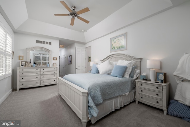 carpeted bedroom with baseboards, visible vents, a raised ceiling, and a ceiling fan