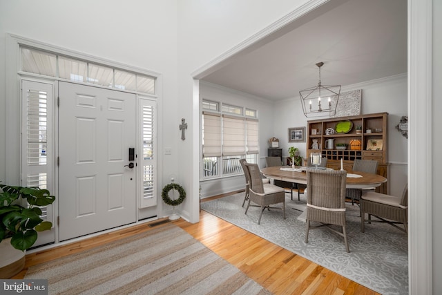 foyer entrance featuring baseboards, visible vents, ornamental molding, wood finished floors, and a notable chandelier