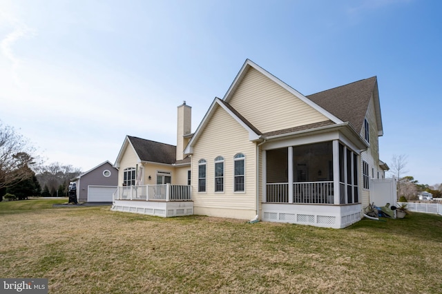 back of property featuring an outbuilding, a yard, a chimney, a sunroom, and a garage