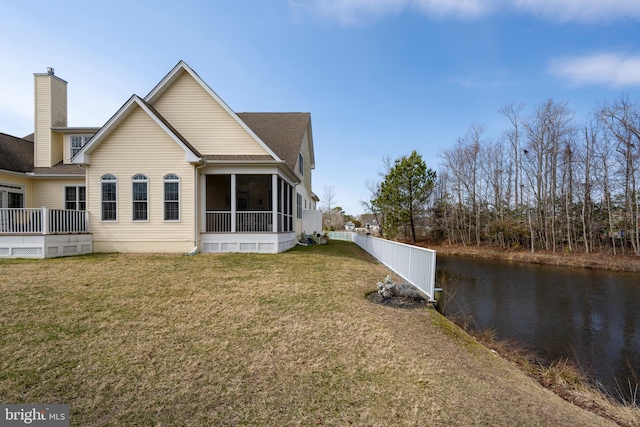 back of house with a sunroom, a chimney, a water view, fence, and a yard