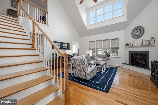 living room with stairs, a glass covered fireplace, a ceiling fan, and wood finished floors