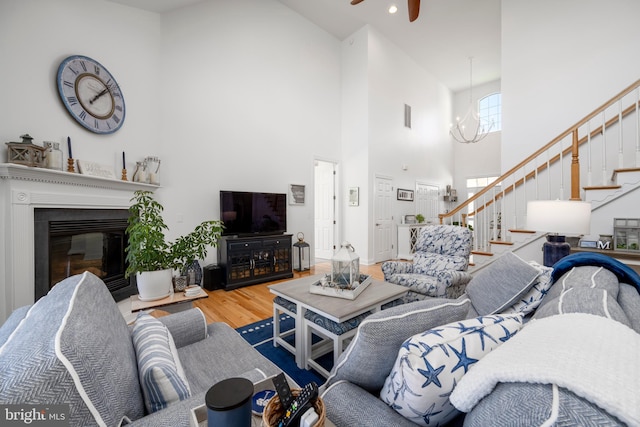 living area featuring a high ceiling, wood finished floors, visible vents, stairs, and a glass covered fireplace