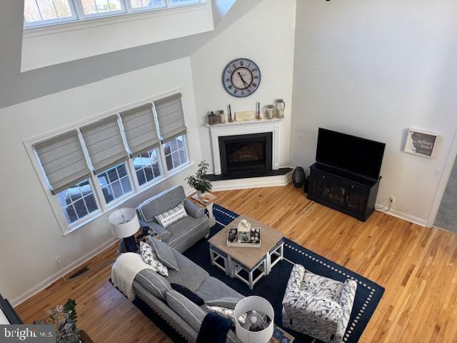 living room featuring a fireplace with raised hearth, wood finished floors, visible vents, and baseboards