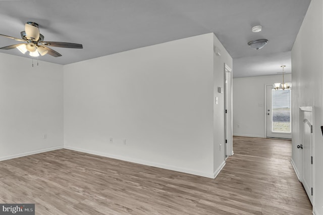 unfurnished room with baseboards, ceiling fan with notable chandelier, and light wood finished floors