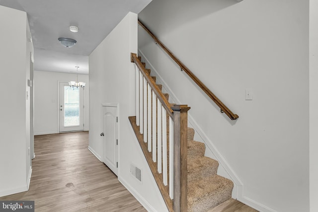 stairway with a notable chandelier, wood finished floors, visible vents, and baseboards