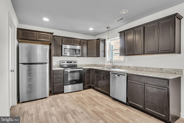 kitchen with light wood-style flooring, a sink, stainless steel appliances, dark brown cabinets, and decorative light fixtures