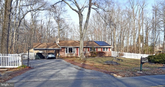 ranch-style house with aphalt driveway, solar panels, fence, a carport, and a chimney