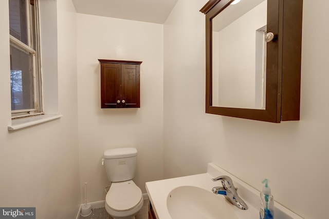 half bath with baseboards, vanity, and toilet