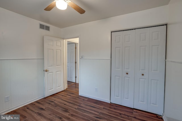 unfurnished bedroom featuring visible vents, dark wood-style floors, ceiling fan, a wainscoted wall, and a closet