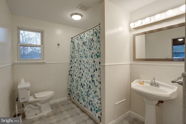 full bath with a wainscoted wall, tile walls, curtained shower, visible vents, and toilet