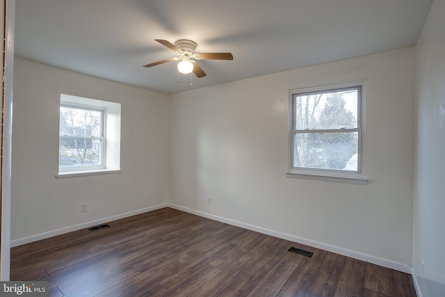 unfurnished room with baseboards, dark wood-type flooring, visible vents, and a healthy amount of sunlight