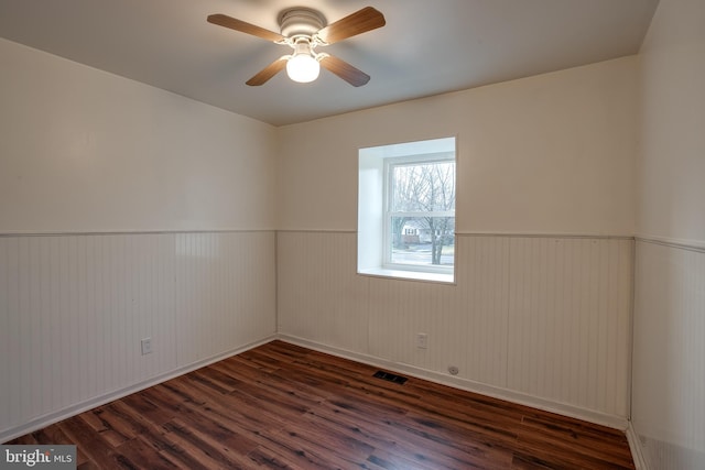 empty room featuring wainscoting, wood finished floors, visible vents, and a ceiling fan