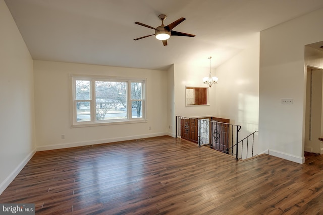 empty room featuring baseboards, vaulted ceiling, dark wood-style flooring, and ceiling fan with notable chandelier