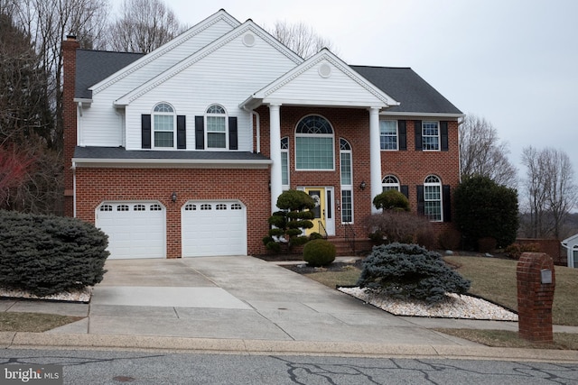 greek revival house with a garage, a chimney, concrete driveway, and brick siding