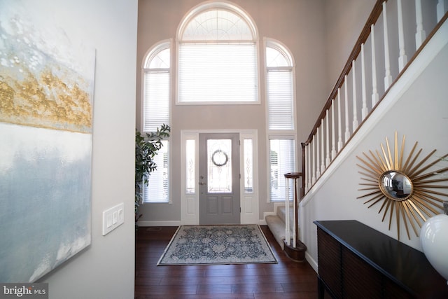 entrance foyer with stairway, dark wood finished floors, a towering ceiling, and baseboards