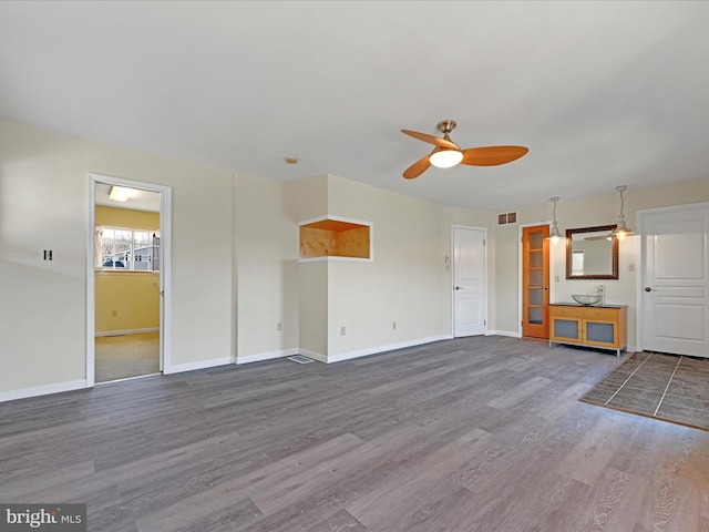 unfurnished living room with ceiling fan, visible vents, baseboards, and wood finished floors