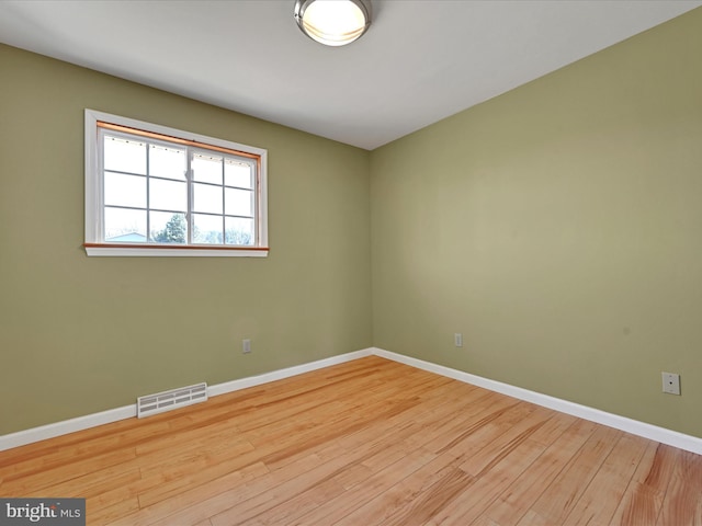 empty room featuring wood finished floors, visible vents, and baseboards