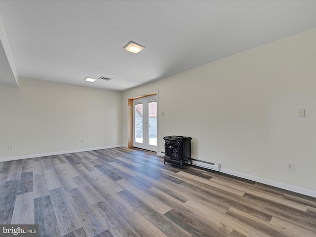 unfurnished room featuring visible vents, a baseboard heating unit, baseboards, a wood stove, and wood finished floors