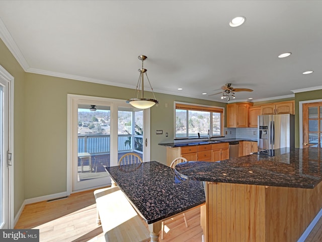 kitchen featuring ornamental molding, light wood-style flooring, stainless steel appliances, decorative backsplash, and baseboards