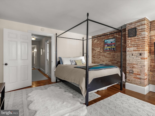 bedroom with baseboards, brick wall, and wood finished floors