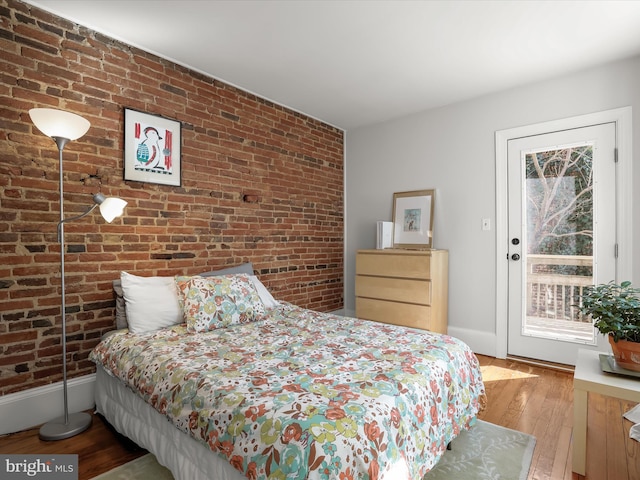 bedroom with access to outside, wood-type flooring, brick wall, and baseboards