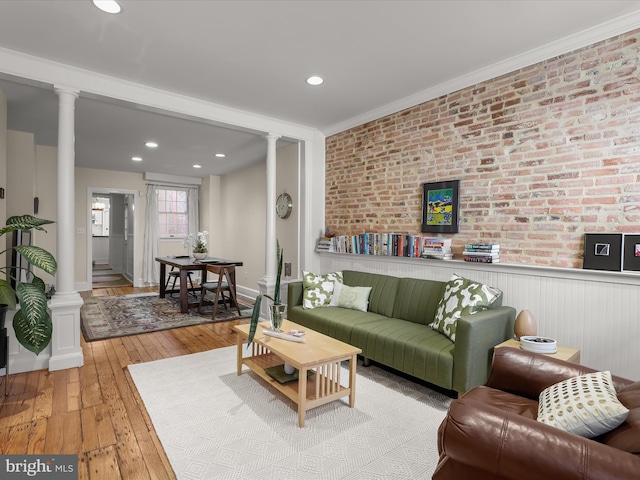 living area featuring a wainscoted wall, decorative columns, ornamental molding, brick wall, and hardwood / wood-style floors