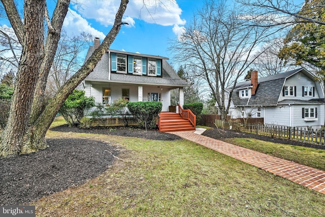 view of front facade with a front yard, fence, a porch, a shingled roof, and a chimney