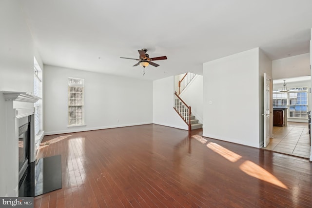 unfurnished living room with wood finished floors, stairway, a glass covered fireplace, and baseboards