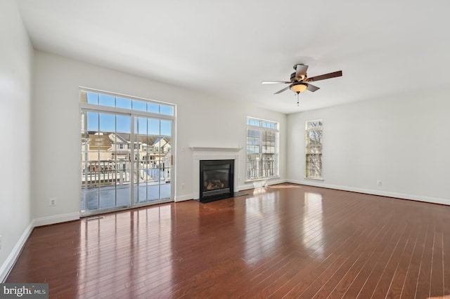 unfurnished living room with a fireplace with flush hearth, dark wood finished floors, baseboards, and ceiling fan