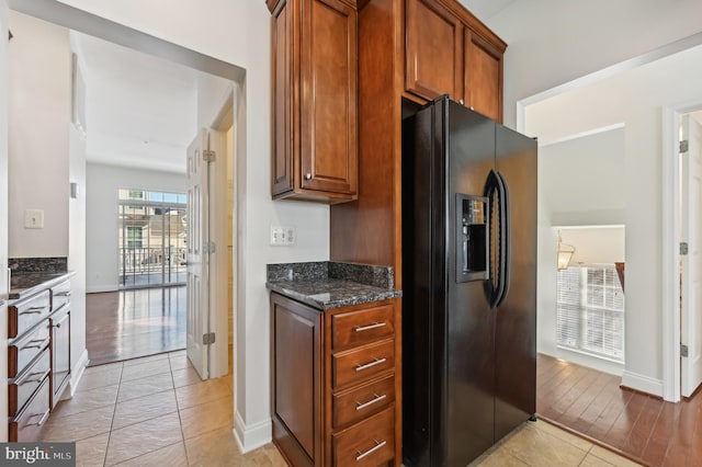 kitchen with baseboards, black fridge with ice dispenser, brown cabinets, dark stone countertops, and light wood-style floors