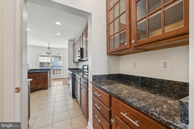 kitchen with appliances with stainless steel finishes, brown cabinetry, glass insert cabinets, and hanging light fixtures