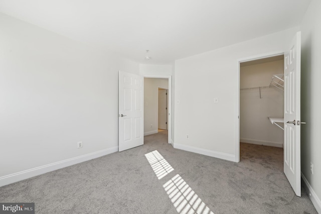 unfurnished bedroom with light carpet, a spacious closet, and baseboards