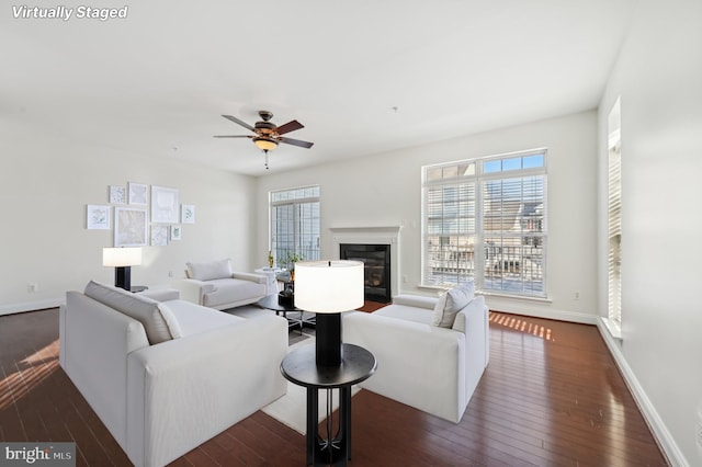 living area featuring a wealth of natural light, a glass covered fireplace, dark wood-style flooring, and baseboards