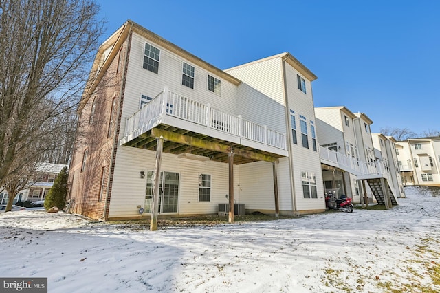 snow covered back of property with a deck, stairway, and central air condition unit