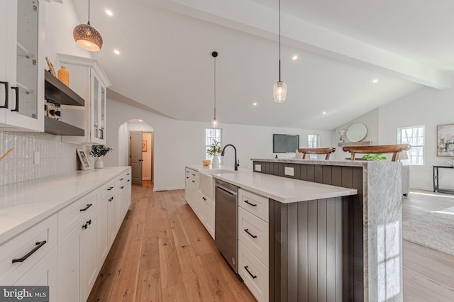 kitchen with lofted ceiling with beams, arched walkways, stainless steel dishwasher, light wood-type flooring, and backsplash