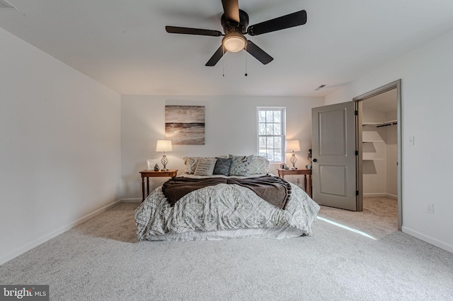 carpeted bedroom with a walk in closet, ceiling fan, and baseboards