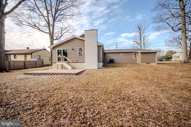 rear view of house featuring entry steps, a chimney, and fence