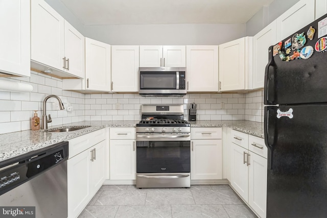 kitchen with white cabinets, light stone counters, stainless steel appliances, and a sink