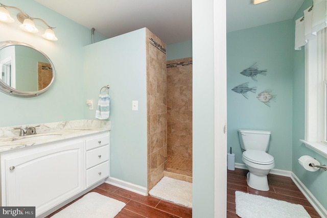 full bath featuring baseboards, wood finish floors, toilet, a tile shower, and vanity