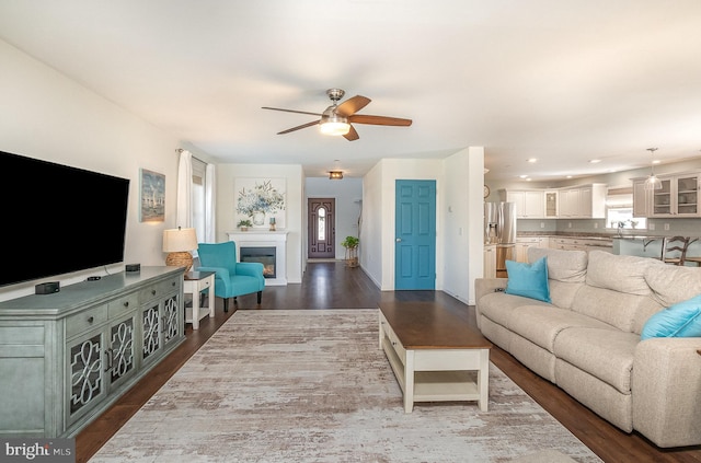 living area featuring ceiling fan, dark wood-type flooring, a glass covered fireplace, and recessed lighting