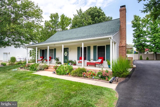 view of front of home featuring covered porch, a chimney, fence, and a front yard