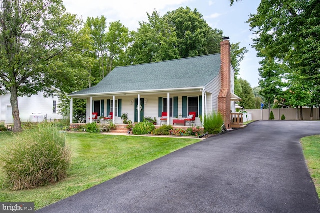 view of front of property featuring roof with shingles, a chimney, a porch, a front yard, and fence