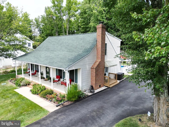 exterior space featuring a front yard, covered porch, roof with shingles, and a chimney