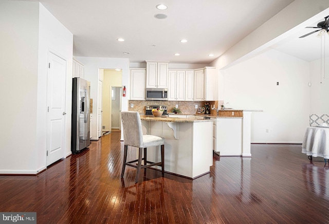 kitchen with light stone counters, a kitchen island, backsplash, stainless steel appliances, and dark wood-style flooring